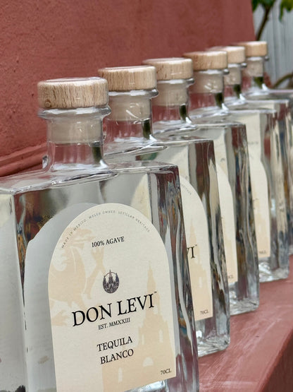 A row of  Don Levi Tequila Blanco with light wood corks and cream labels, lined up against a terracotta-colored wall.