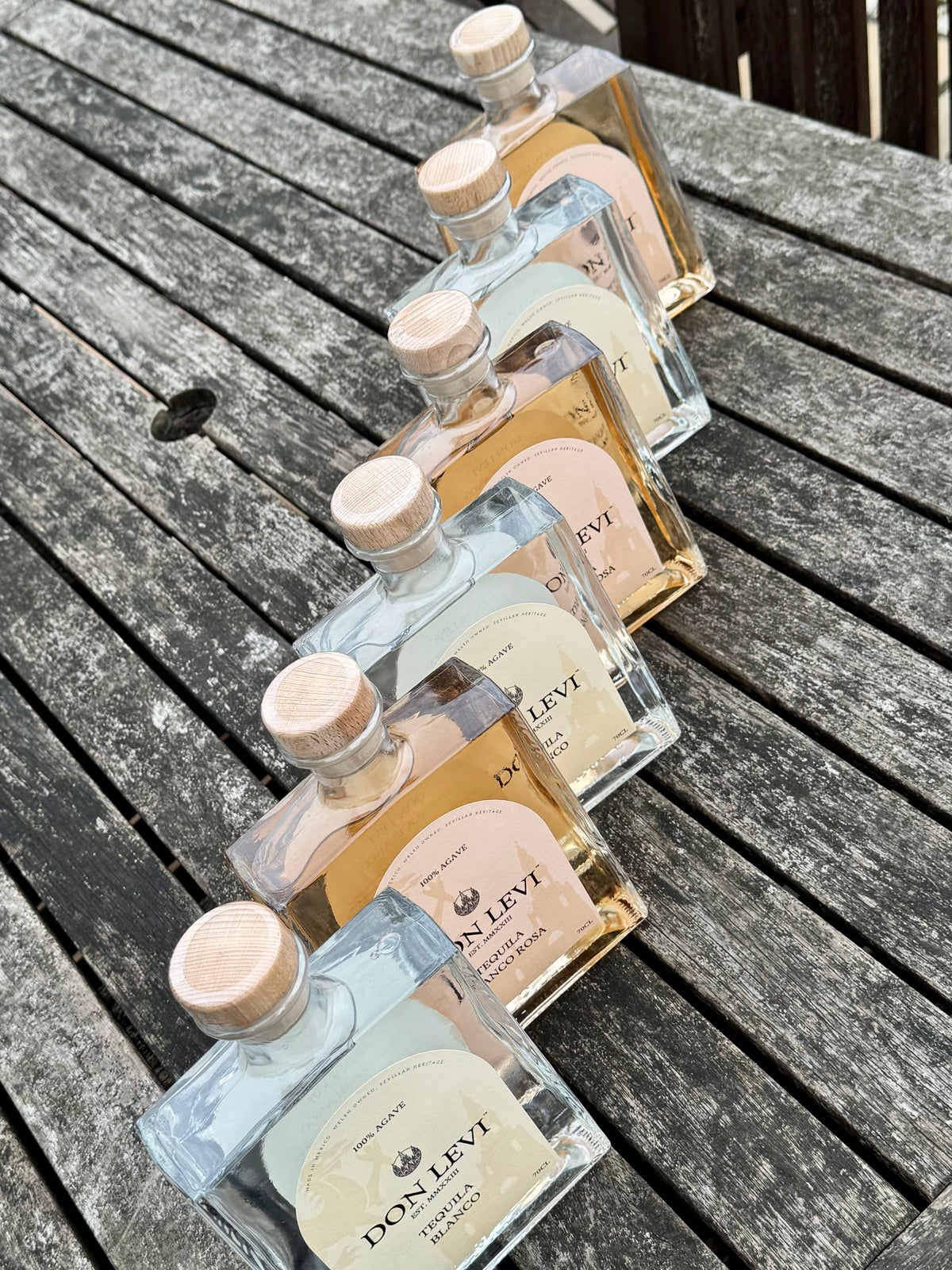 3 bottles of Don Levi Blanco & Rosa on a wooden, weathered table.