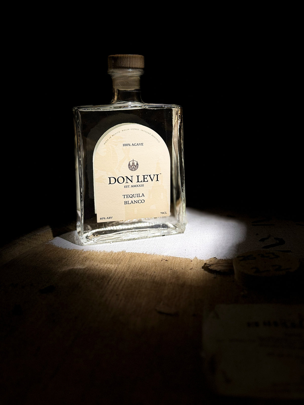 Bottle of Don Levi Blanco in a dim light room on a wooden barrel with some illuminating light on the bottle. 